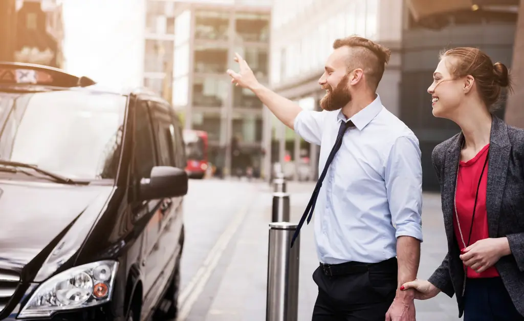 Driver opening the rear door of a black car for two passengers